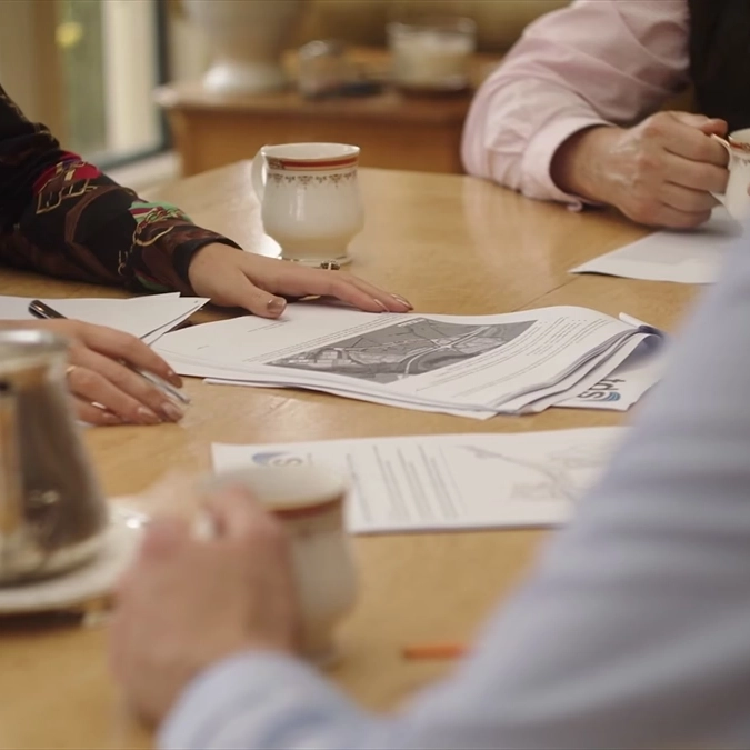 Close-up of a meeting discussing site plans, with papers, pens and tea on the table.