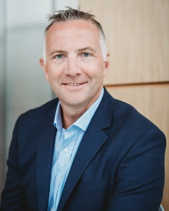 Group finance director in a navy suit and light blue striped shirt, smiling in a modern office