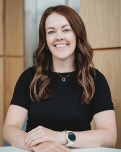 Planning manager seated at a table, smiling in a modern office with wood-panel backdrop