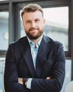 Senior land manager in a navy suit and light blue shirt, arms crossed in a bright, modern office