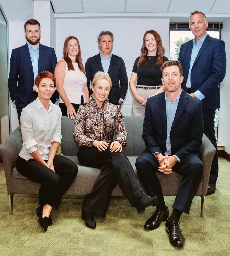 Nine-person team group portrait in a modern office, seated and standing around a sofa