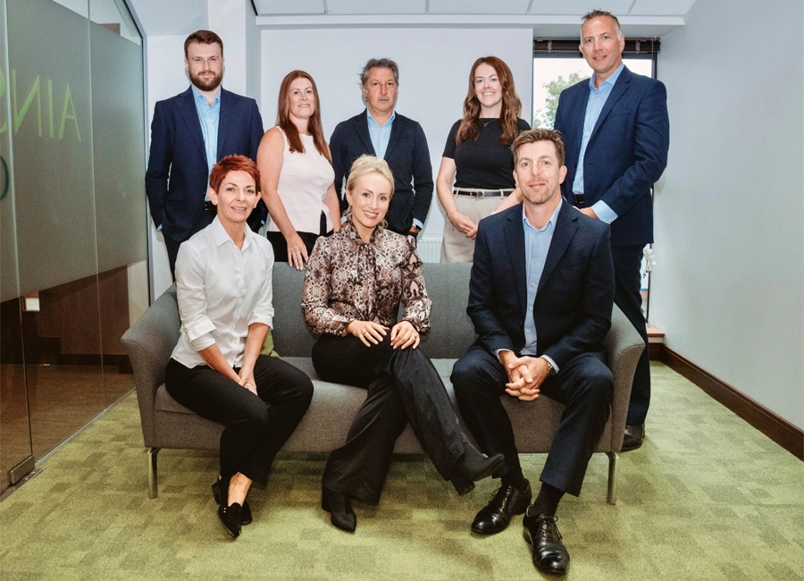 Nine-person team group portrait in a modern office, seated and standing around a sofa